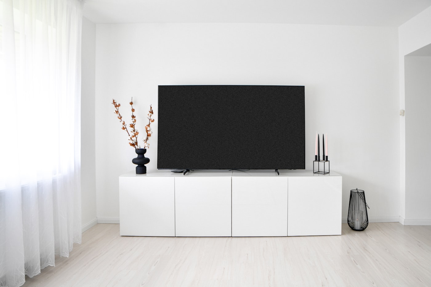 Laag wit tv-meubel tegen een lichte muur met een vaas en kandelaars