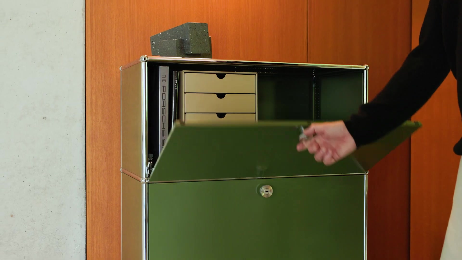 Olijfgroene USM Haller-kast met klep en lades tegen een houten wand